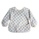Mushie long sleeve bib in blue check protects outfits during meals.
