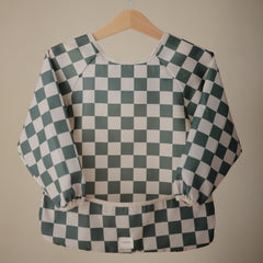 Mushie long sleeve bib olive check pocket close-up shows crumb-catching feature for mess-free meals.