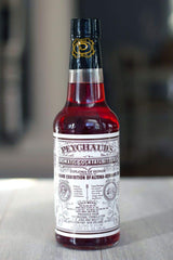 Peychaud's bottle with glass and ice demonstrates versatile use in cocktails.