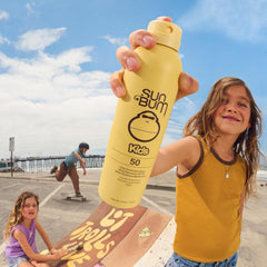 Sun Bum Kids SPF 50 Clear Spray being applied to hands before face for even coverage.