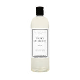 The Laundress Darks Detergent bottle pour showing stain-fighting care for vibrant darks