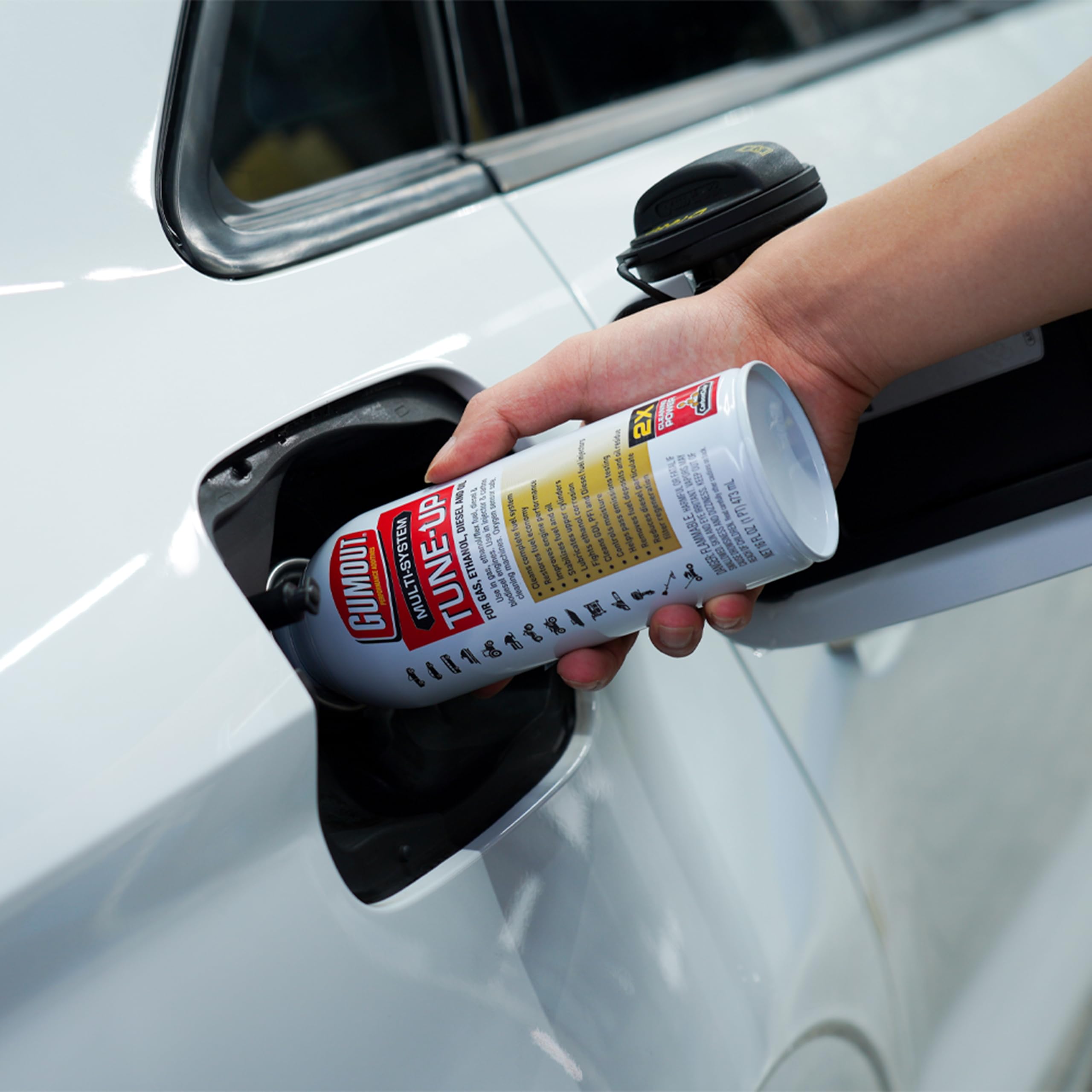 Gumout Multi-System Tune-Up bottle being poured into fuel tank for cleaner system.
