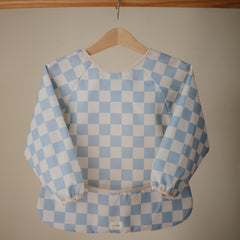 Mushie blue check bib pocket catches crumbs during mealtime.