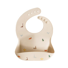 Mushie silicone baby bib with dinosaurs pattern and deep pocket catches crumbs.