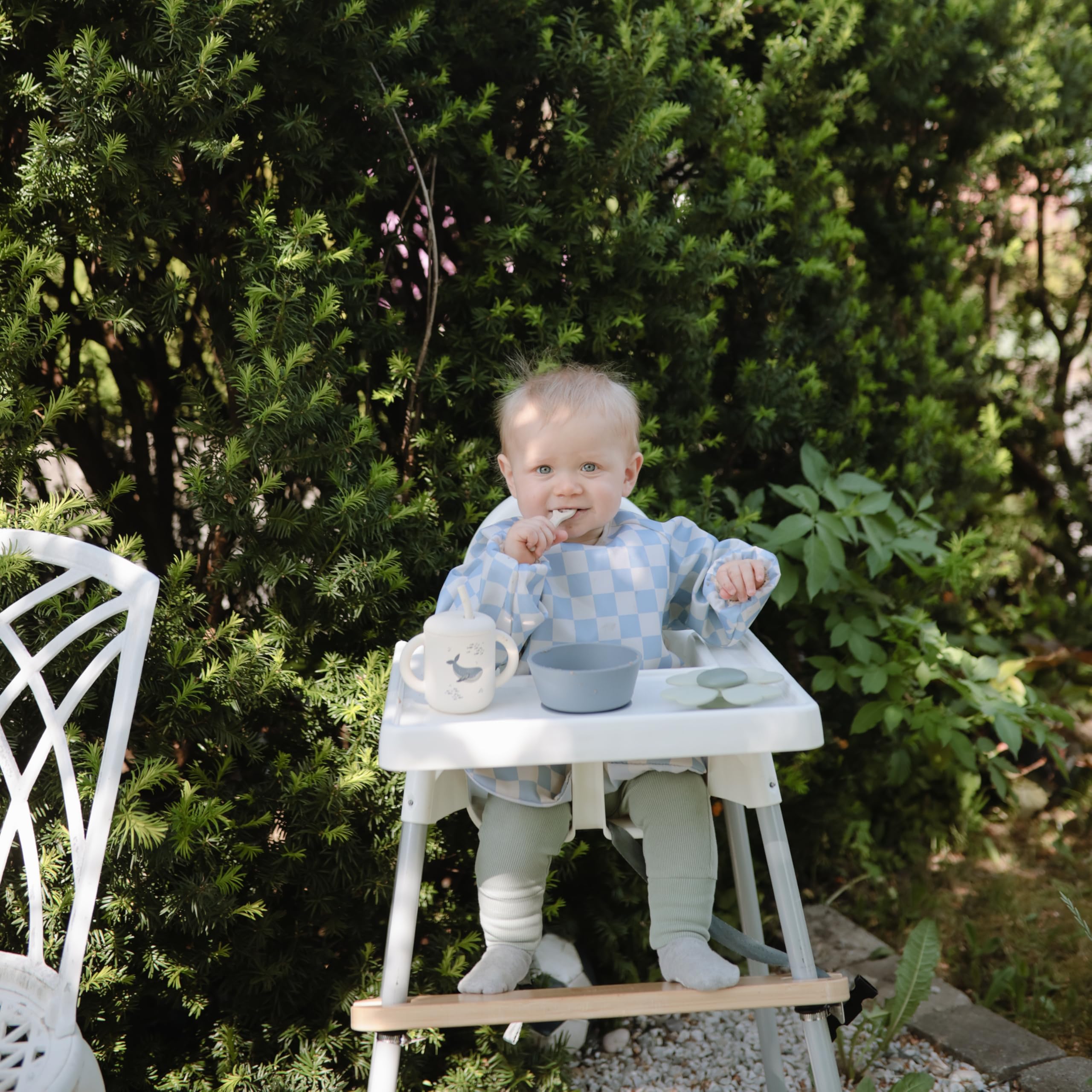 Mushie long sleeve bib olive check worn by baby during meals to minimize stains.