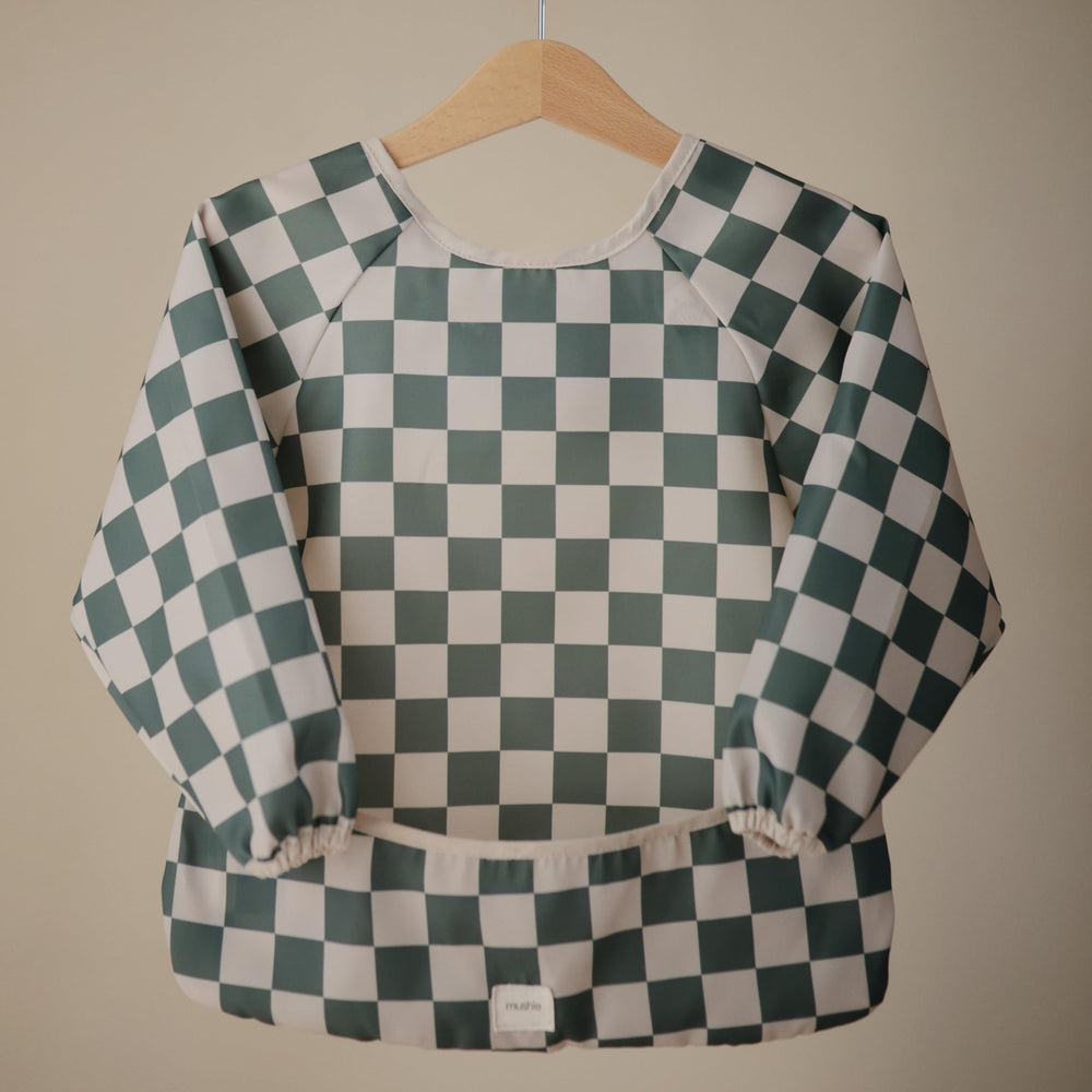 Mushie long sleeve bib olive check pocket close-up shows crumb-catching feature for mess-free meals.