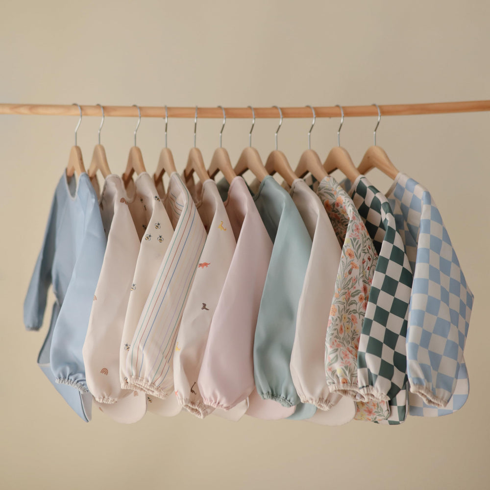 Mushie long sleeve bib with Velcro neck illustrates easy adjustable fit for 6–24 months.