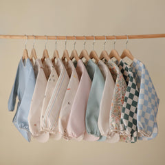 Mushie long sleeve bib with Velcro neck illustrates easy adjustable fit for 6–24 months.