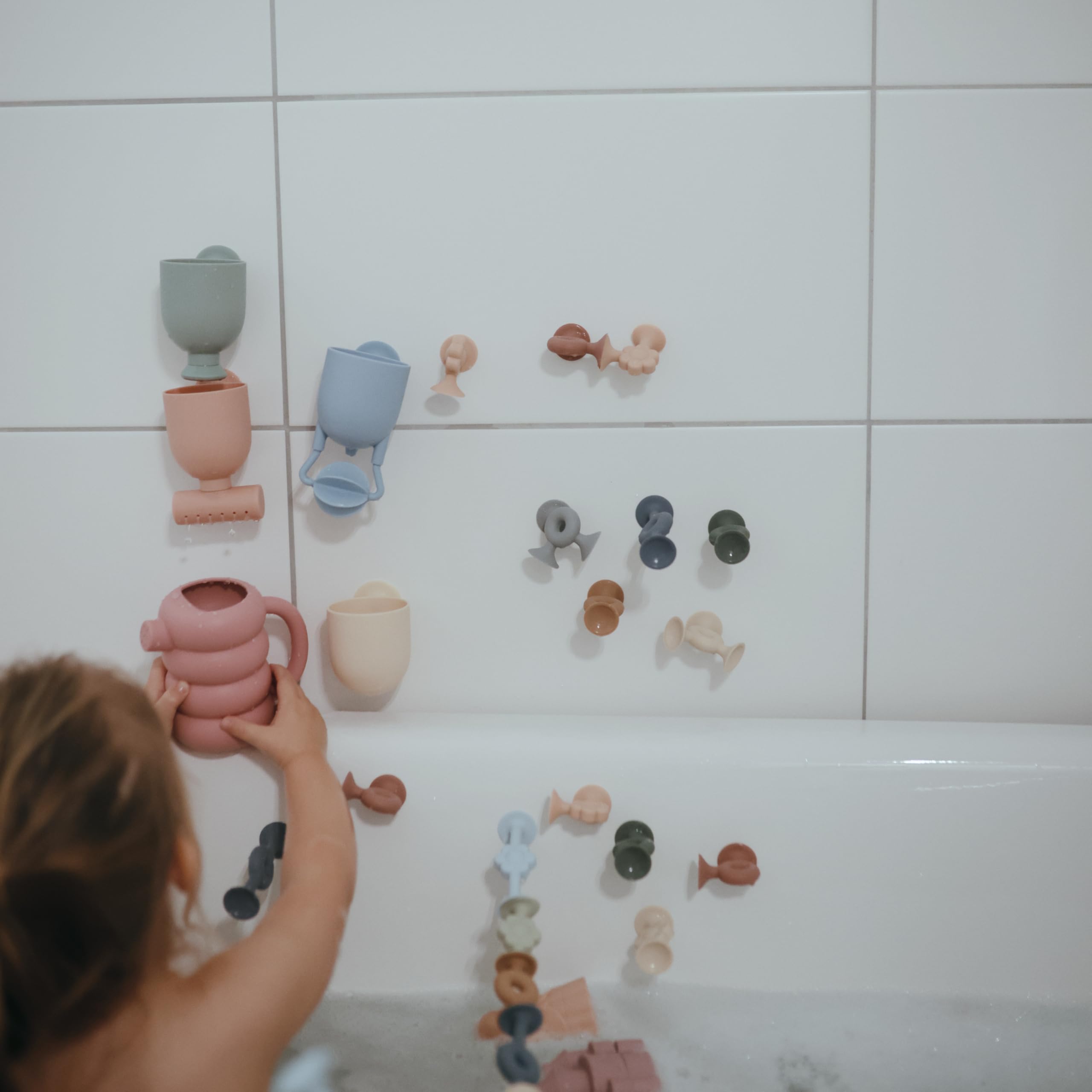 Mushie bath toy with suction cups mounted on tub wall for safe waterfall play.