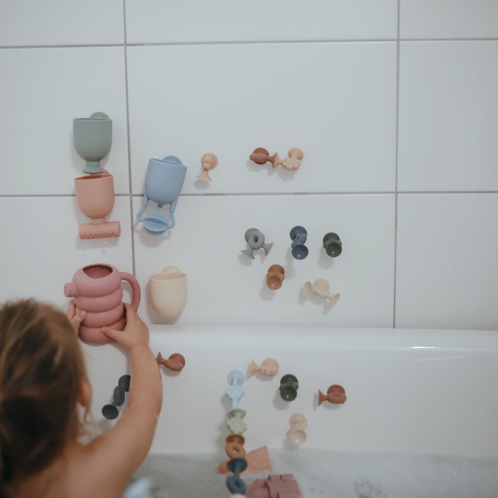 Mushie bath toy with suction cups mounted on tub wall for safe waterfall play.
