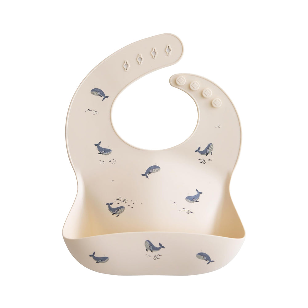 Mushie silicone baby bib with adjustable fit in whales pattern for mess-free mealtimes.