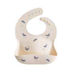 Mushie silicone baby bib with adjustable fit in whales pattern for mess-free mealtimes.