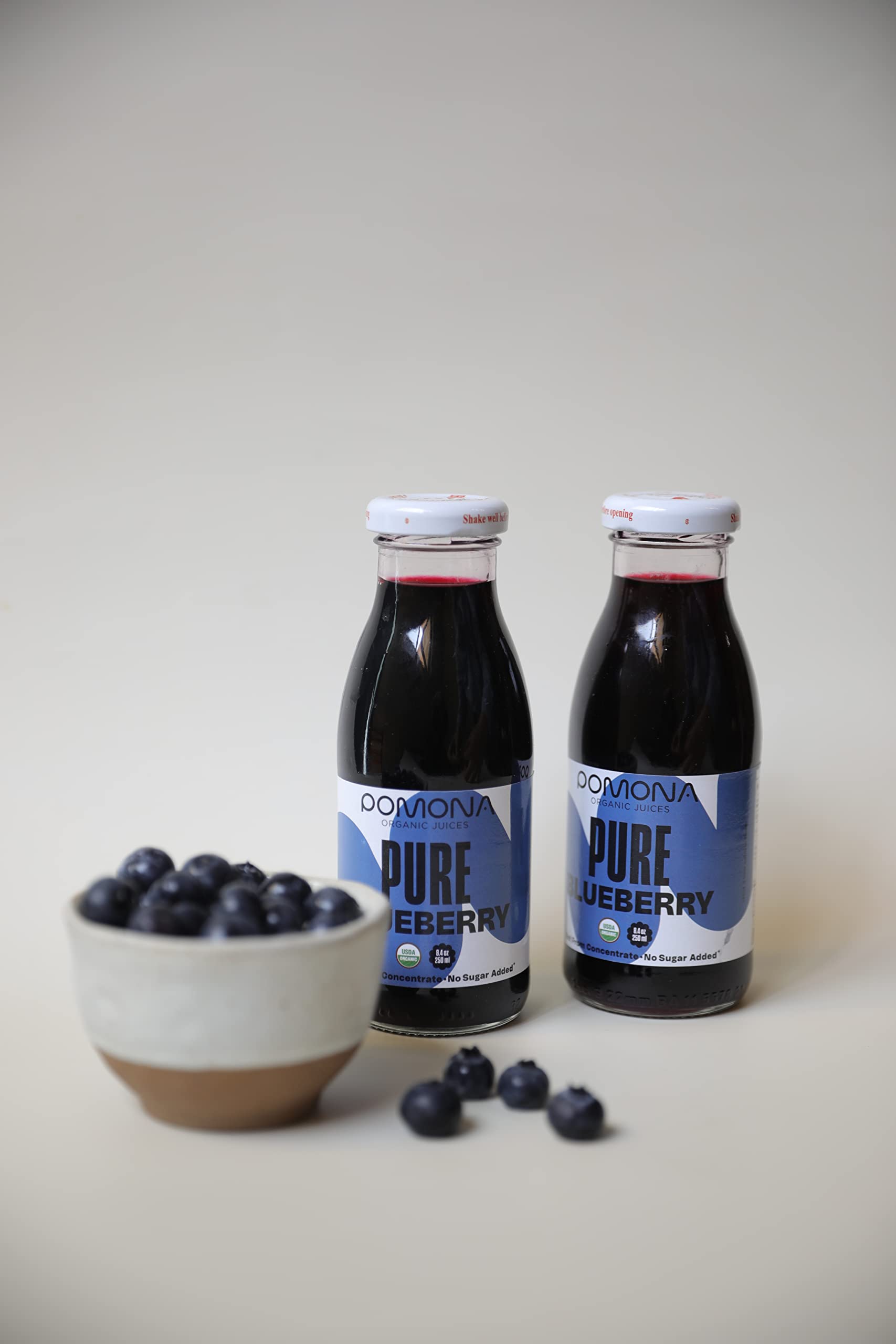 Pomona Blueberry Juice bottle on wood conveys natural, wholesome flavor appeal.