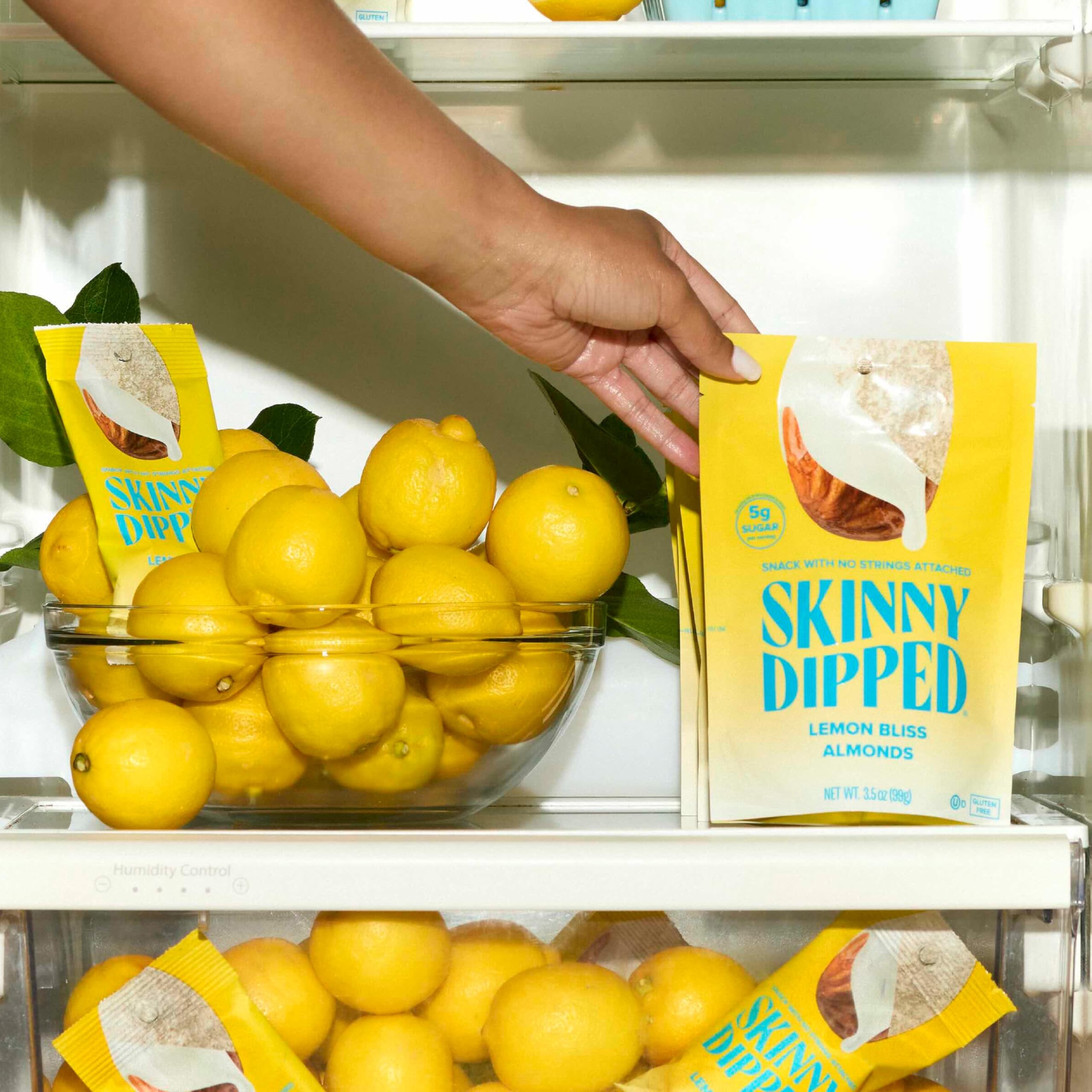 SkinnyDipped Lemon Bliss Almonds hand holding a mini-pack for busy days.