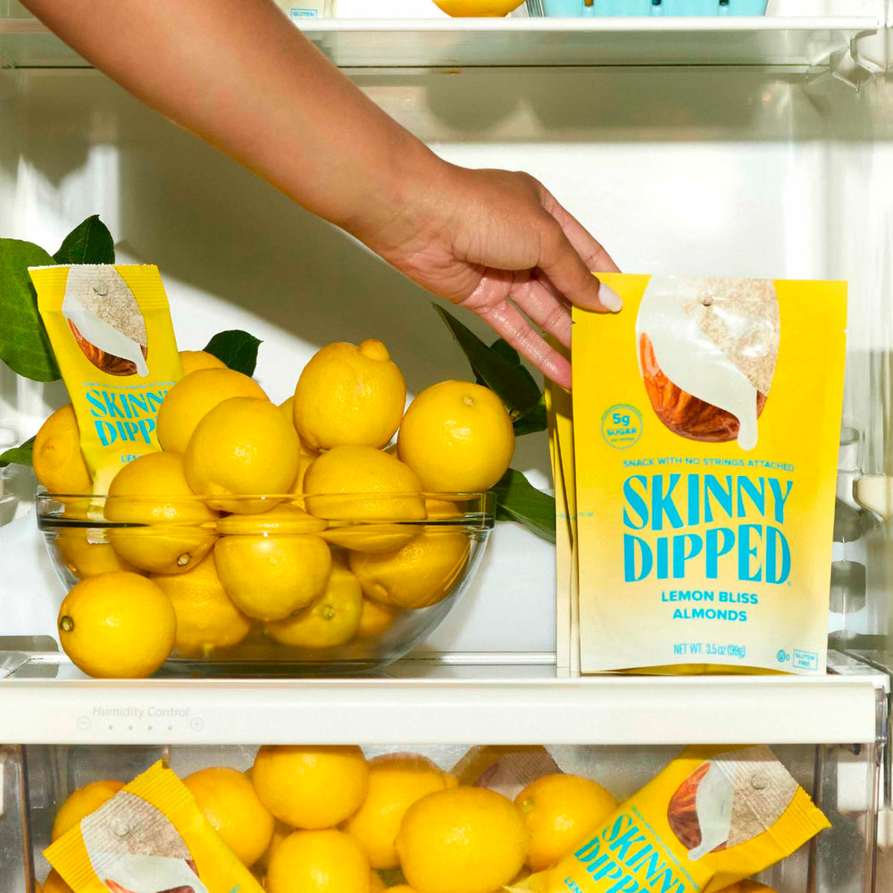 SkinnyDipped Lemon Bliss Almonds hand holding a mini-pack for busy days.