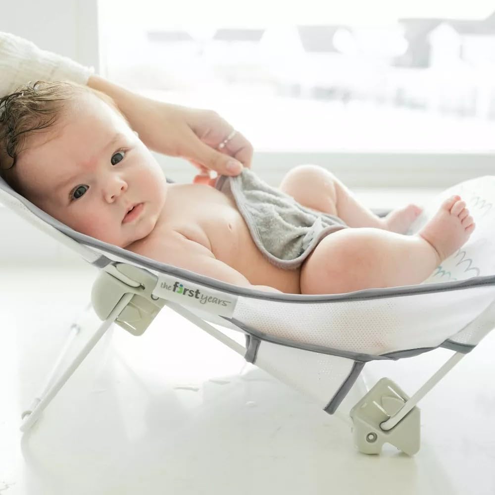 The First Years Sure Comfort folding bather in tub, gentle incline cradling baby.