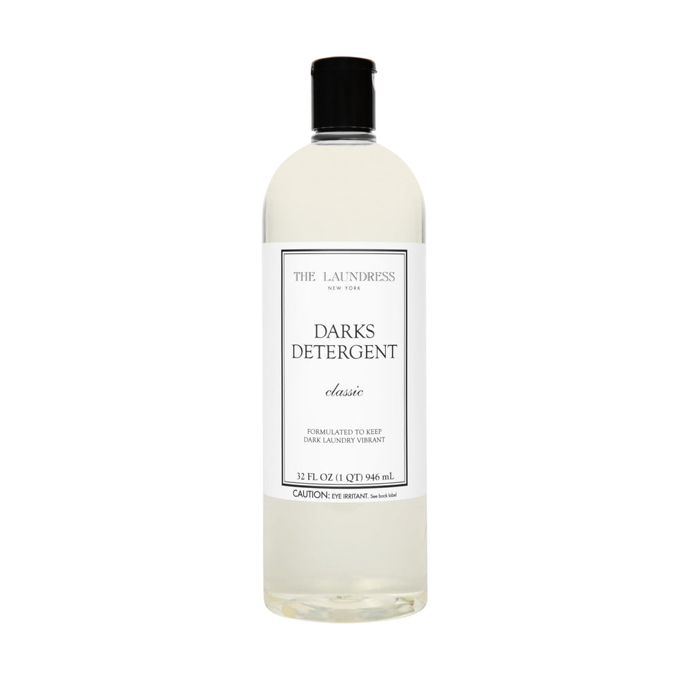 The Laundress Darks Detergent bottle pour showing stain-fighting care for vibrant darks